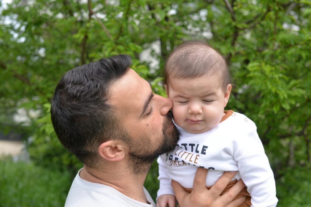 Father kissing baby in a tender moment outdoors, portraying love and fatherhood.