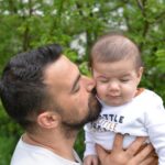 Father kissing baby in a tender moment outdoors, portraying love and fatherhood.