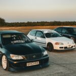 Three customized sports cars parked on open asphalt under a clear sky.