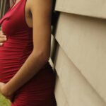 Elegant maternity photo featuring a pregnant woman in a red dress outdoors.