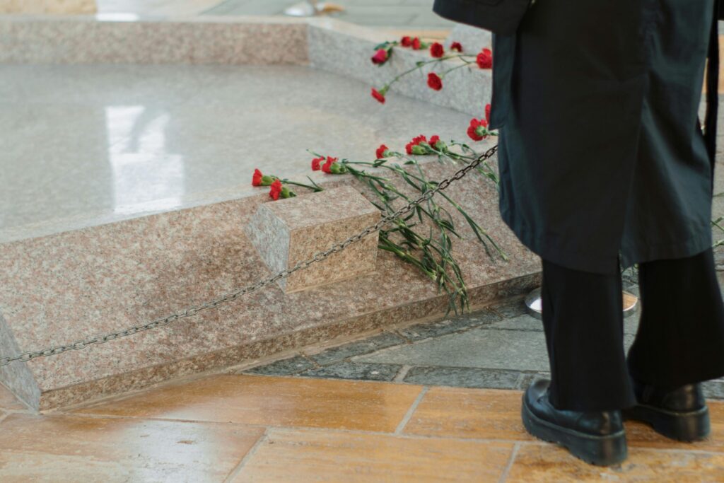 Close-up of a grave with red roses during a memorial ceremony, featuring a man's presence.