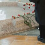 Close-up of a grave with red roses during a memorial ceremony, featuring a man's presence.