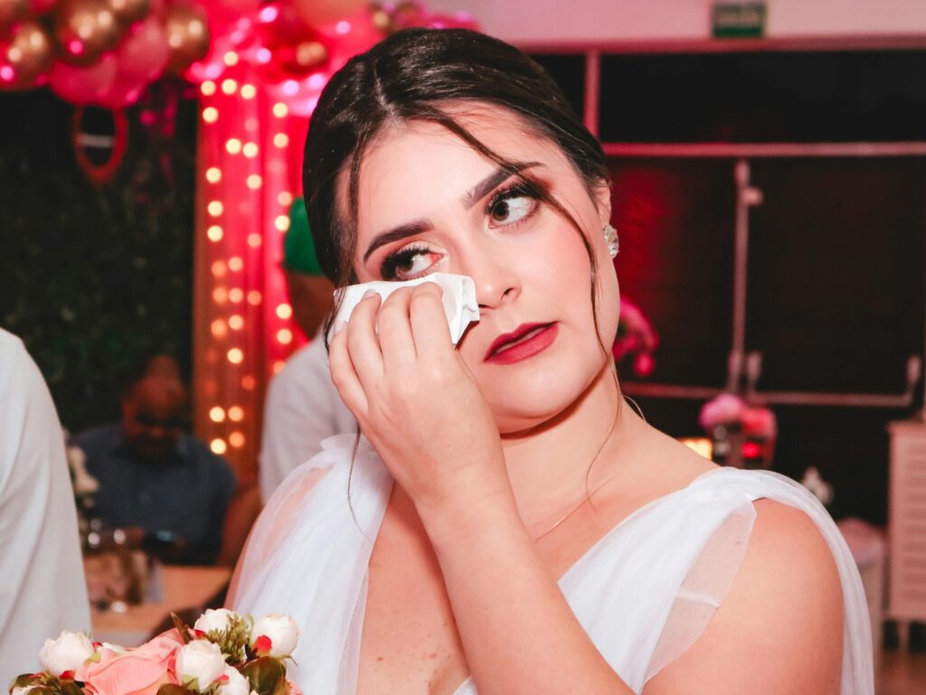 Bride wipes tears of joy while holding a bouquet during a heartfelt moment at her wedding.