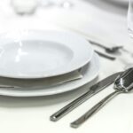 Elegant dining table with white porcelain plates and silver cutlery elegantly arranged.