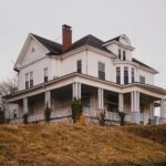 Beautiful historic white house with a wraparound porch set against autumn surroundings.