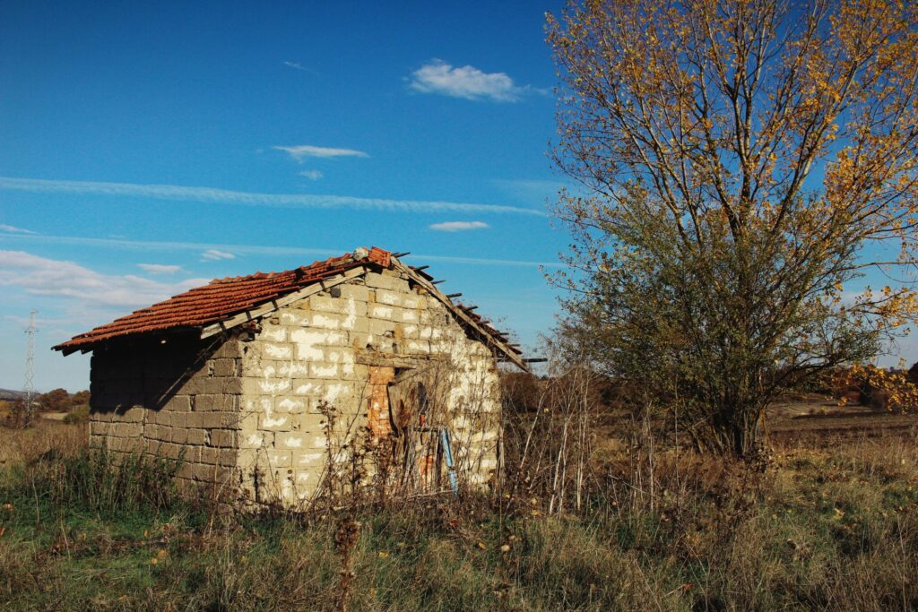 Abandoned stone house with red roof in a rural autumn landscape.