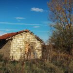 Abandoned stone house with red roof in a rural autumn landscape.