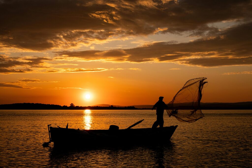 Dramatic sunset silhouette of a fisherman casting a net on a lake in Bursa, Türkiye, creating a serene and peaceful scene.