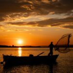 Dramatic sunset silhouette of a fisherman casting a net on a lake in Bursa, Türkiye, creating a serene and peaceful scene.