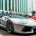 Luxury silver sports car parked in front of modern glass facade building.