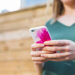 Woman using a smartphone with a colorful case outside on a sunny day.