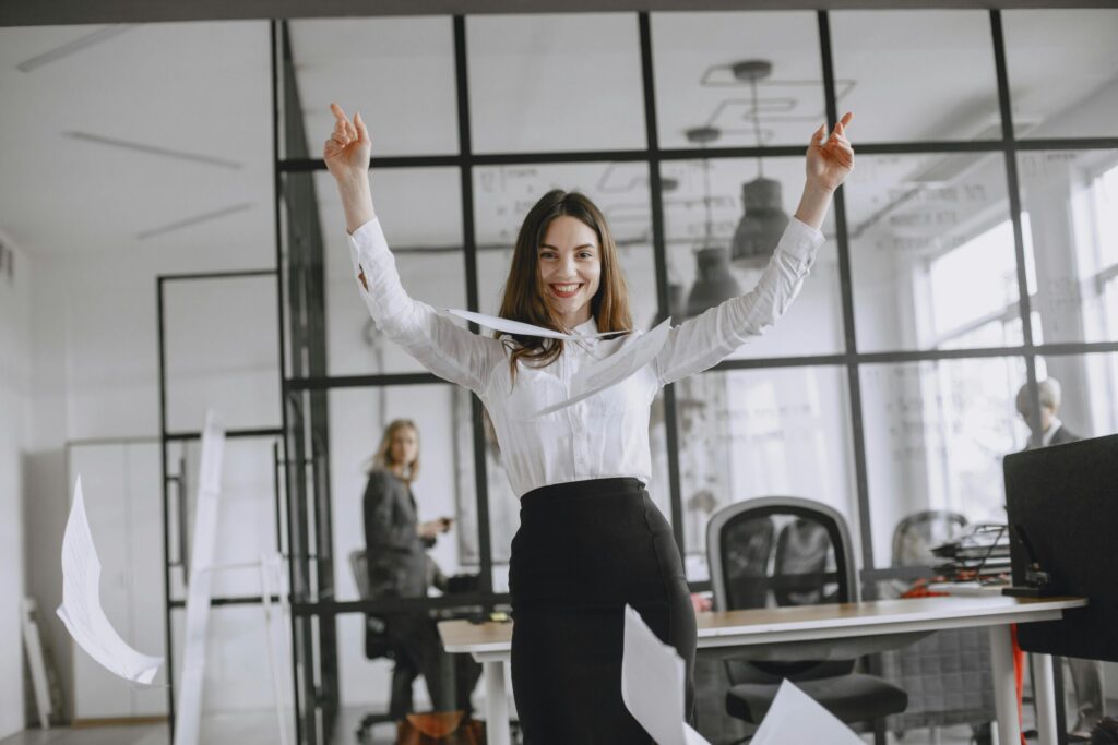 Smiling businesswoman in a modern office throws papers in the air, expressing joy and success.