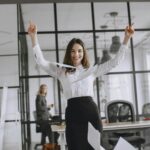 Smiling businesswoman in a modern office throws papers in the air, expressing joy and success.