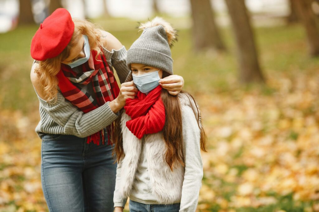 Woman and child wearing face masks in a park during fall, highlighting protective care.