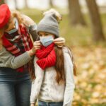 Woman and child wearing face masks in a park during fall, highlighting protective care.