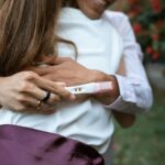Couple sharing a heartfelt embrace holding a positive pregnancy test outdoors.