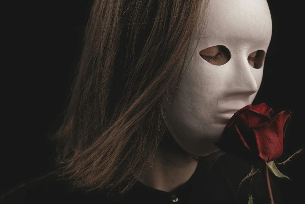 Mysterious portrait of a person with a white mask holding a red rose. Dark and intriguing mood.