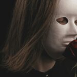 Mysterious portrait of a person with a white mask holding a red rose. Dark and intriguing mood.