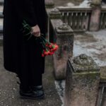 A somber scene of a person holding red flowers near a tombstone at a cemetery.