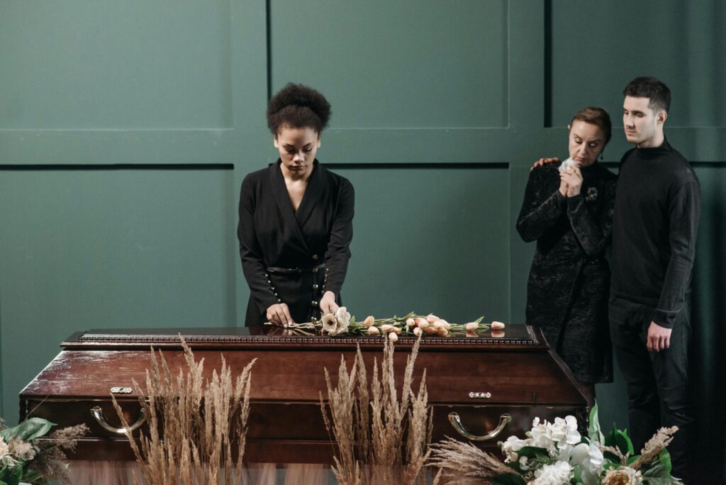 A heartfelt funeral scene indoors featuring grieving adults and a coffin adorned with flowers.