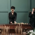A heartfelt funeral scene indoors featuring grieving adults and a coffin adorned with flowers.
