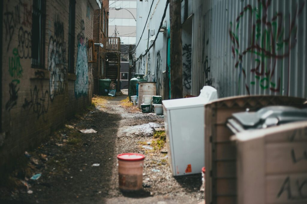Empty narrow street with trash cans and garbage on ground near shabby walls with graffiti in daytime