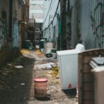 Empty narrow street with trash cans and garbage on ground near shabby walls with graffiti in daytime