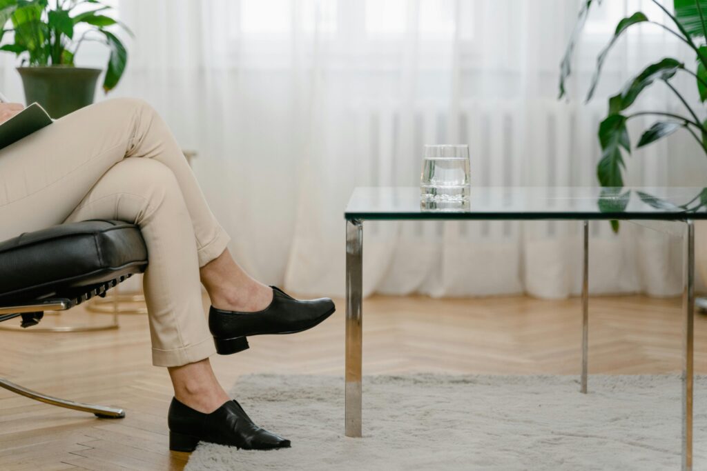 A person relaxes in a modern living room with beige pants and a glass of water on a table.