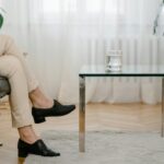 A person relaxes in a modern living room with beige pants and a glass of water on a table.