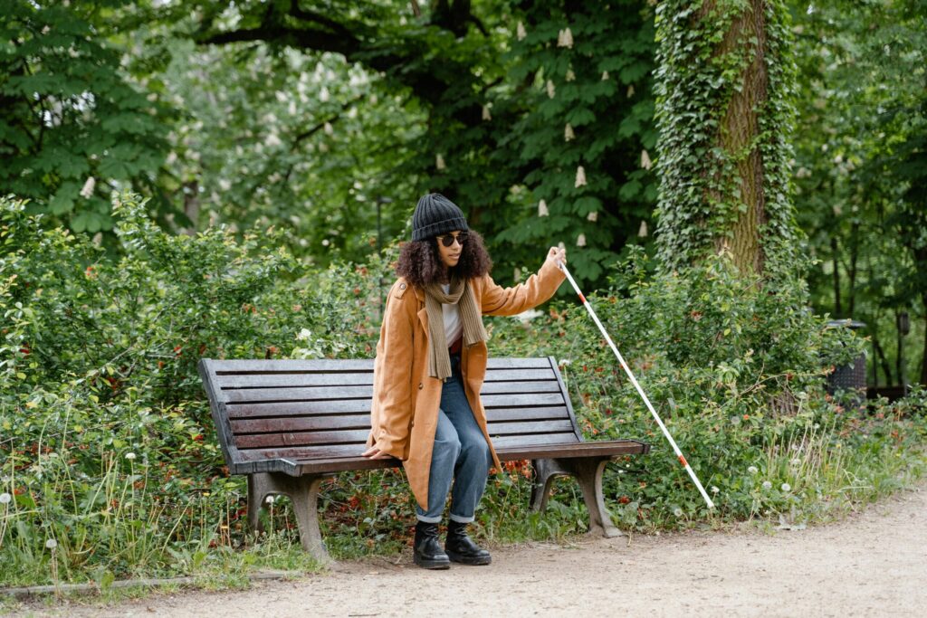 African American woman with visual impairment using white cane by park bench.