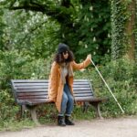 African American woman with visual impairment using white cane by park bench.