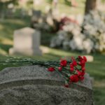 Red carnations placed on a headstone in a peaceful green cemetery during the day.