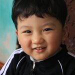 Cute child smiling warmly at the camera indoors with vibrant background.