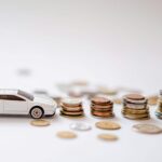 White toy sports car beside stacks of coins on a white background, emphasizing savings and finance.